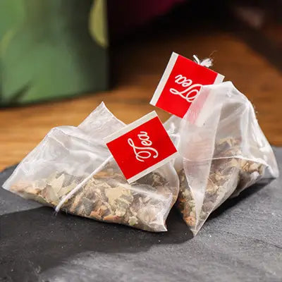 Two pyramid-shaped herbal tea bags with lotus leaf promoting intestinal motility during golden hour