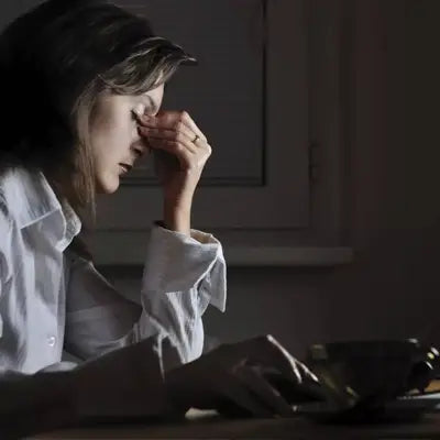 Stressed woman at desk drinking herbal tea during golden hour to manage irregular diet