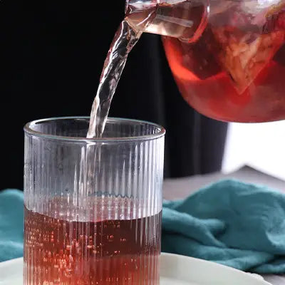 Ribbed glass being filled with red herbal tea infused with pina date seed to enhance sleep quality